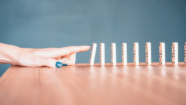 hand pushing dominoes in a line on wooden table