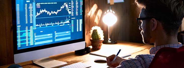 businessman taking notes while looking at data metrics on computer screen