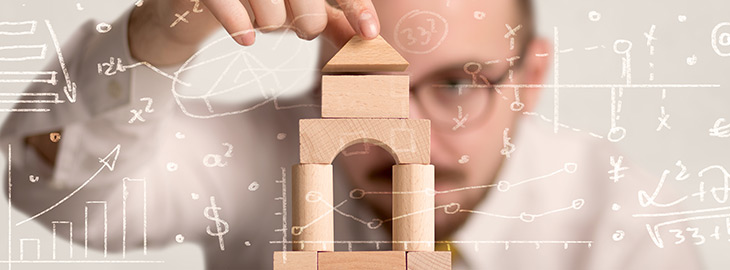 Young businessman using wooden building blocks with white calculations scribbled around him