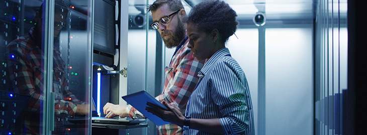 man and woman with tablet using laptop in server room while checking servers