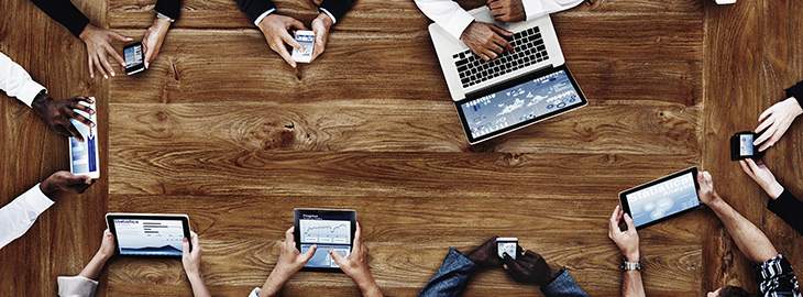 business people using multiple digital devices sitting at a conference table