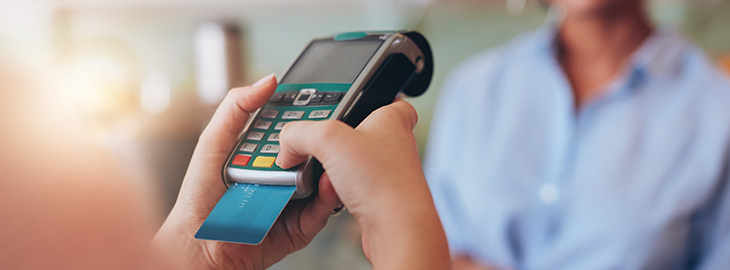 Young woman paying by credit card at juice bar. Focus on woman hands entering security pin in credit card reader.