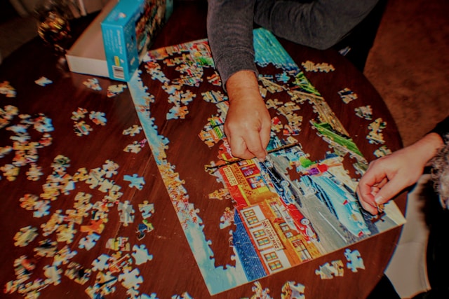two people putting puzzle pieces together on wooden table