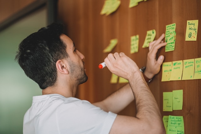 person writing on colorful sticky notes on wooden wall