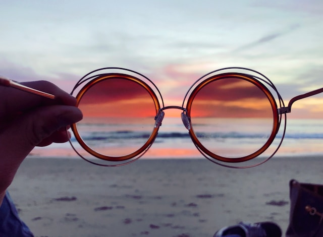 red circular sunglasses focused on a sunset over the ocean line